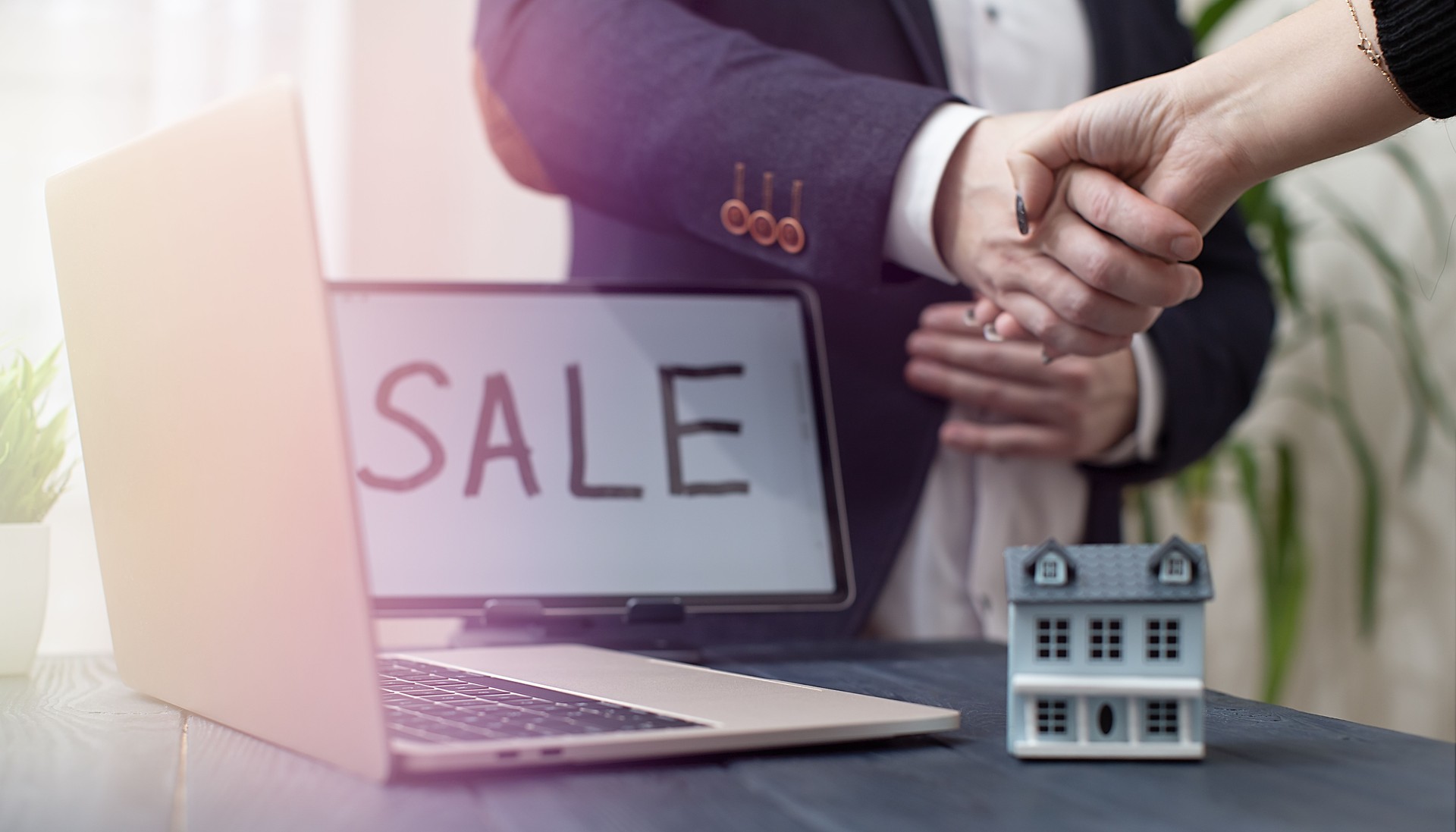 Handshake Agreement in Real Estate Sale with Laptop and Model House on Desk
